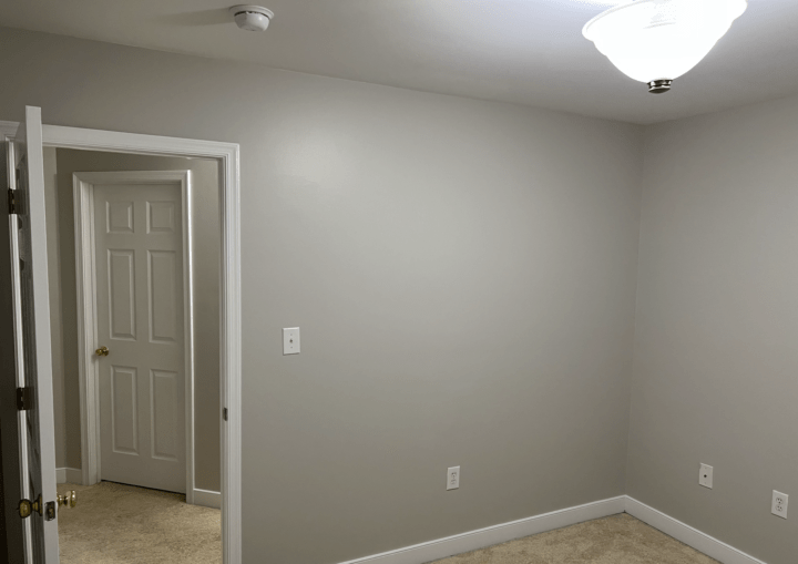 A bedroom with grey walls, white trim, and beige carpet
