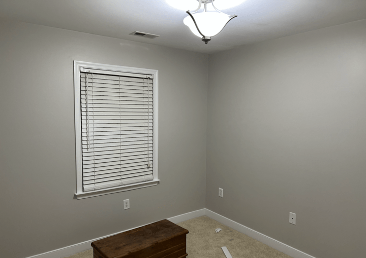 A bedroom with grey walls, white trim, and beige carpet