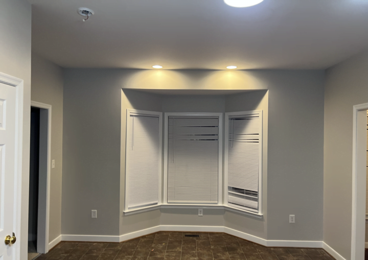 A room with a bay window, grey walls, and white trim