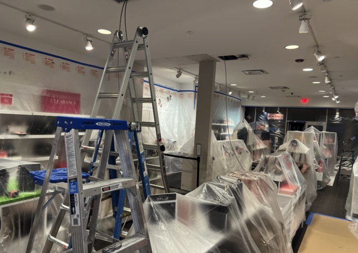 A man prepares a storeroom for painting by covering the purses and products with plastic