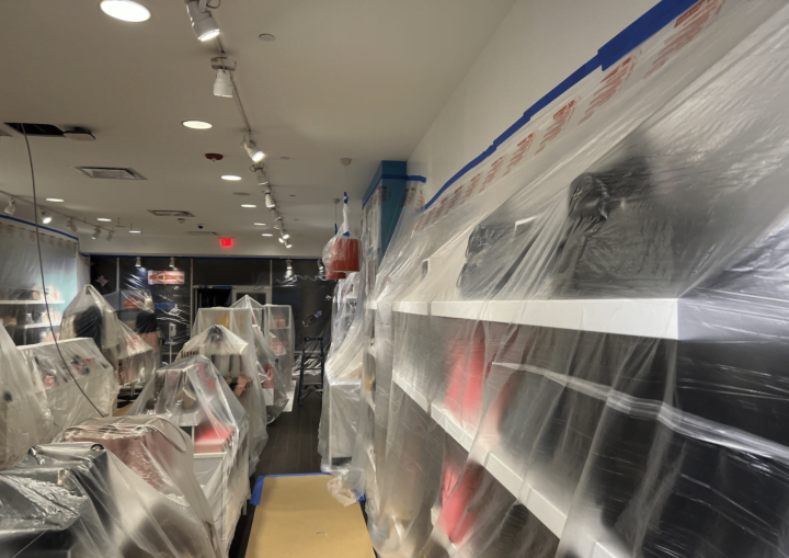 A man prepares a storeroom for painting by covering the purses and products with plastic