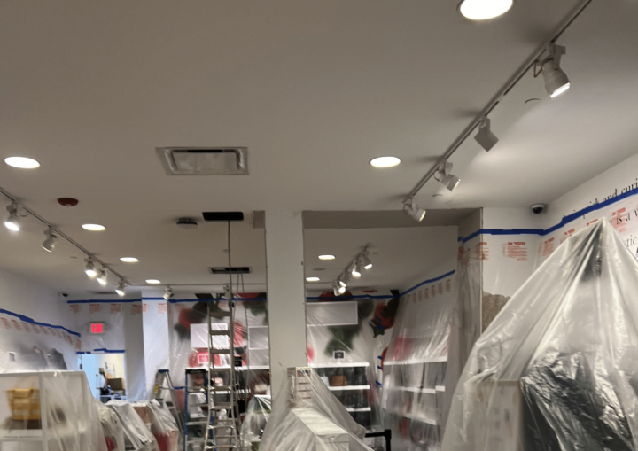 A man prepares a storeroom for painting by covering the purses and products with plastic