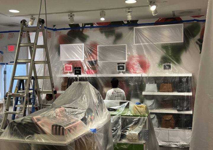 A man prepares a storeroom for painting by covering the purses and products with plastic