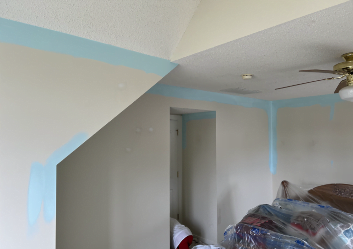 A man works to paint the trim and corners of a room light blue