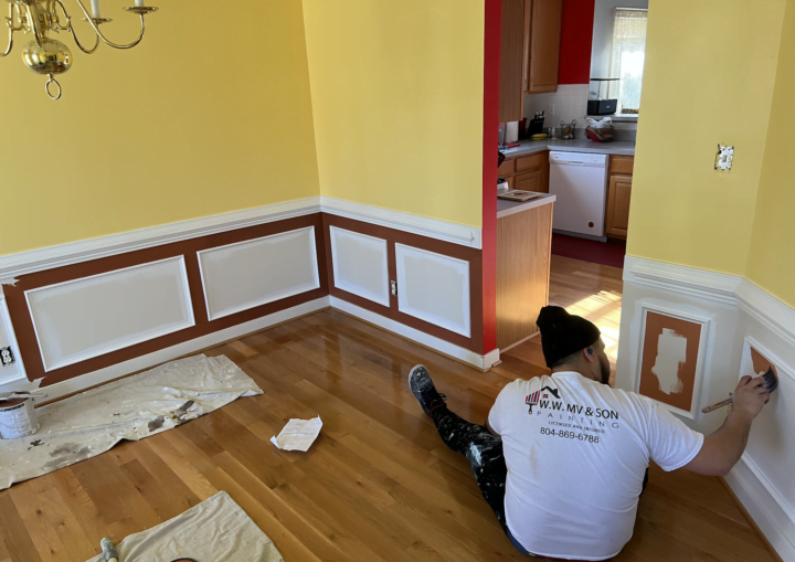 A man paints a room with red paint below the chair rail and yellow above