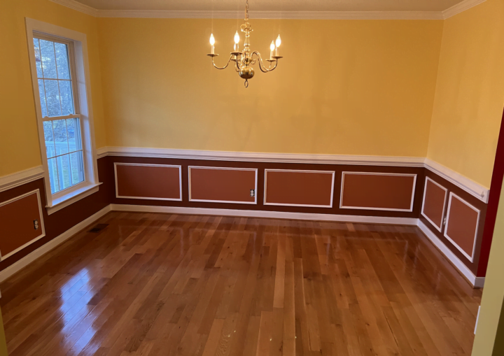 A dining room with red below the chair rail and yellow above