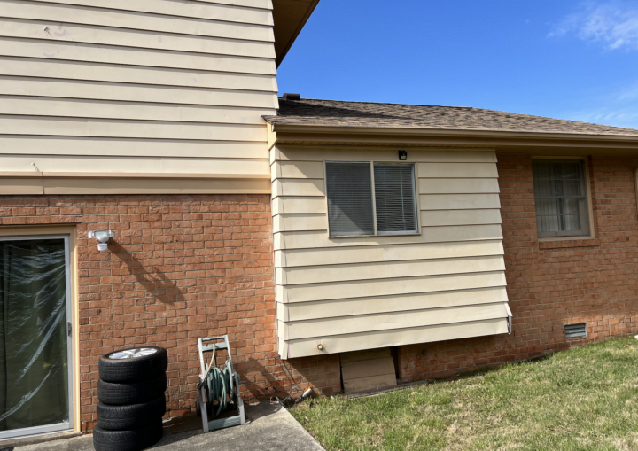 The outside of a house with siding and bricks against a blue sky