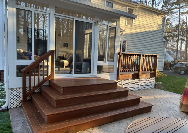 A wooden deck leads to a sunroom with white trim and siding