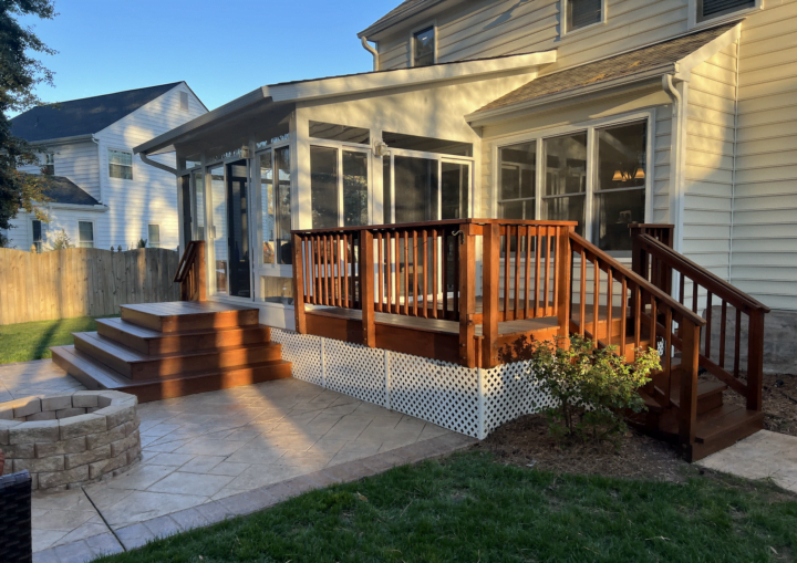 A wooden deck leads to a sunroom with white trim and siding