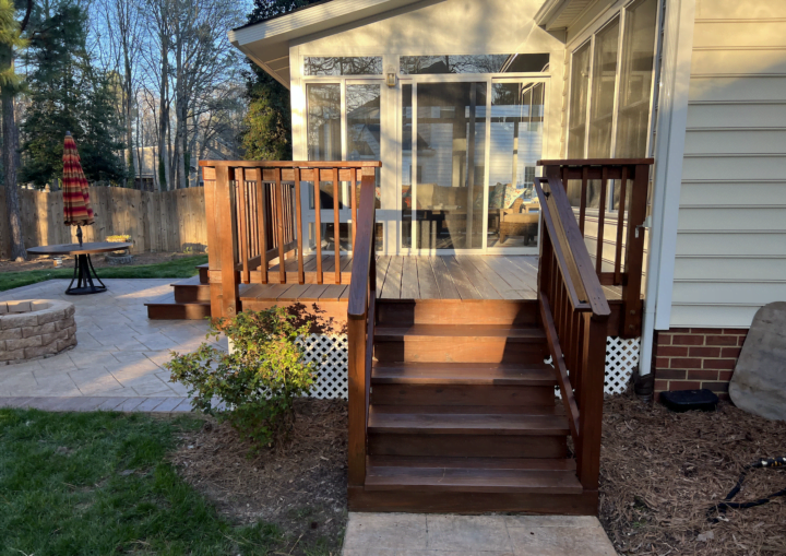 A wooden deck leads to a sunroom with white trim and siding