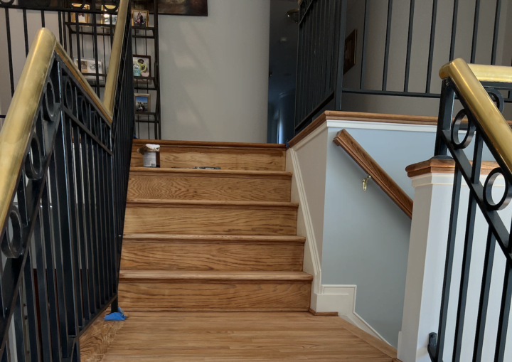 Blue painters' tape lines the base of a wrought iron handrail on a wooden staircase