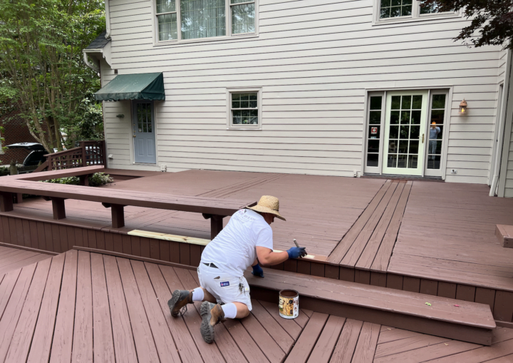 A man in a sunhat paints a wooden deck