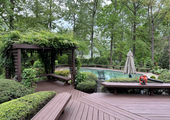 A freshly painted brown deck and trellis with greenery in the background