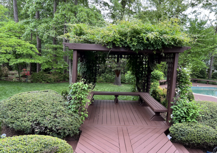 A freshly painted brown deck and trellis with greenery in the background