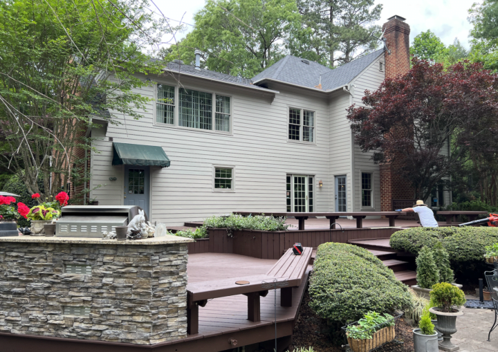 A two story house with white paint with a deck being painted in the foreground