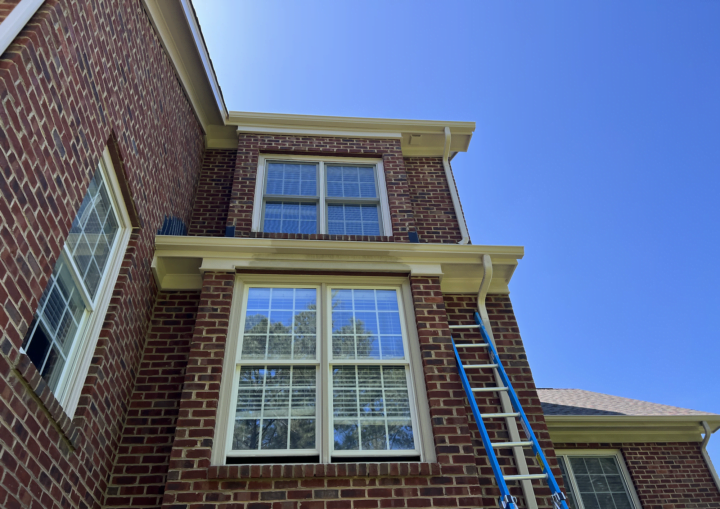 A ladder leans up agains a brick house with blue painters' tape around the windows