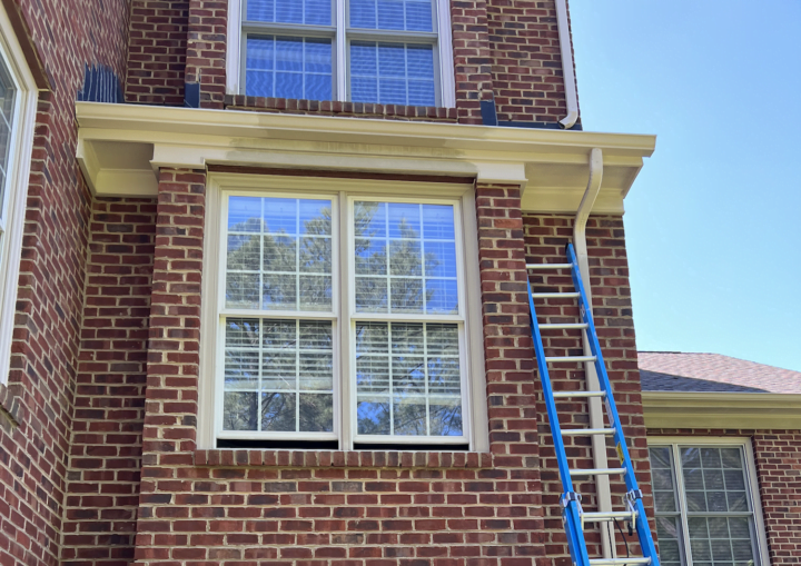 A ladder leans up agains a brick house with blue painters' tape around the windows