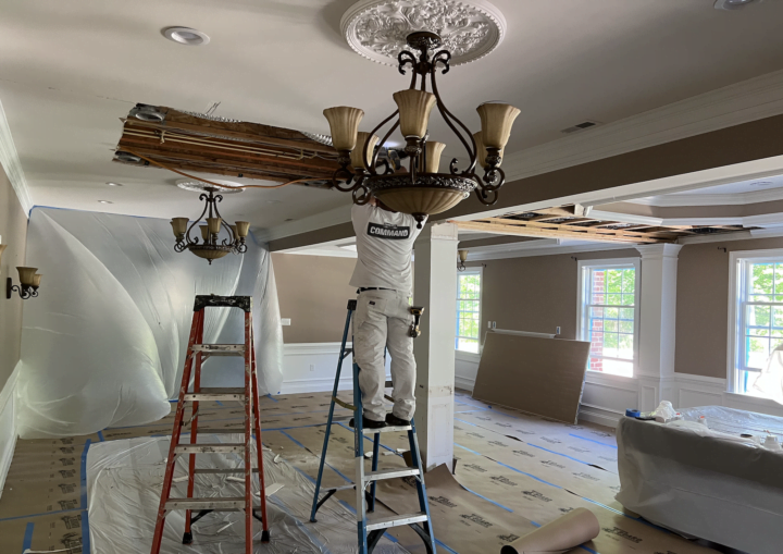 A man stands on a ladder preparing the ceiling fixtures for painting