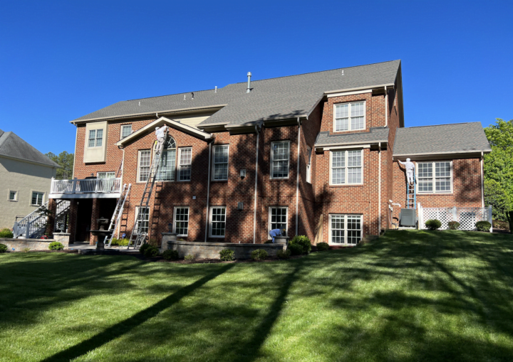 Men on tall ladders work to paint the trim on the outside of a brick house