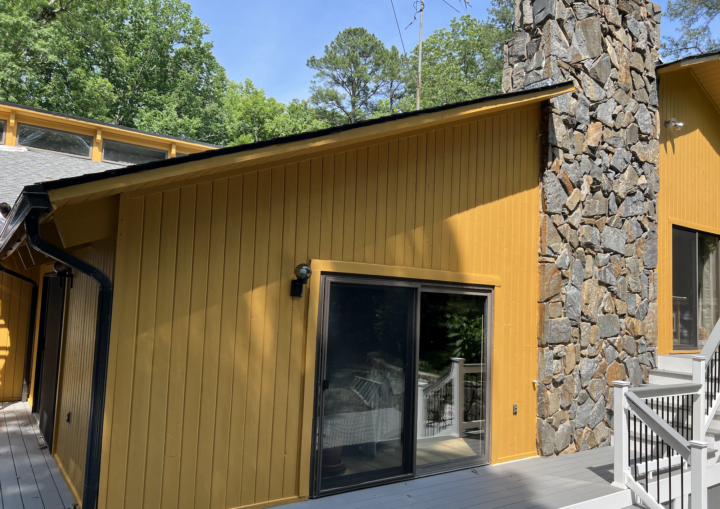 The outside of a freshly painted, modern house in a goldenrod color with large glass windows