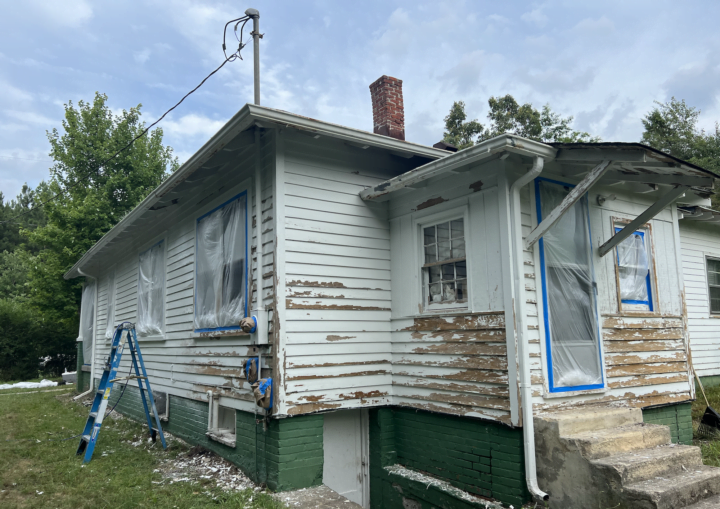 A house with chipped and peeling siding is prepped for painting