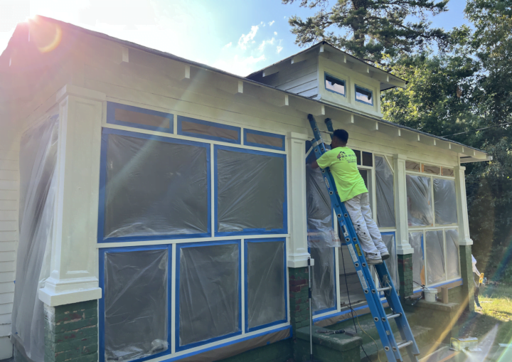 A man prepares the outside of a house for painting by covering the windows in plastic and painters' tape