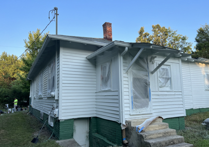A bungalow house is prepped for painting with windows covered by protective plastic