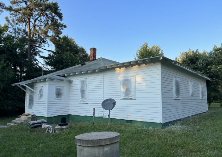 A bungalow house is prepped for painting with windows covered by protective plastic