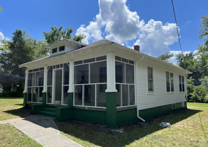 A one story bungalow house with white siding and green trim