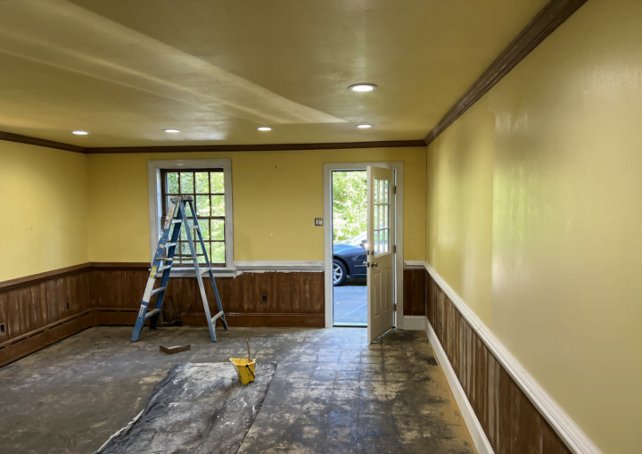A yellow room and yellow ceiling with brown trim and a ladder in the middle of the room