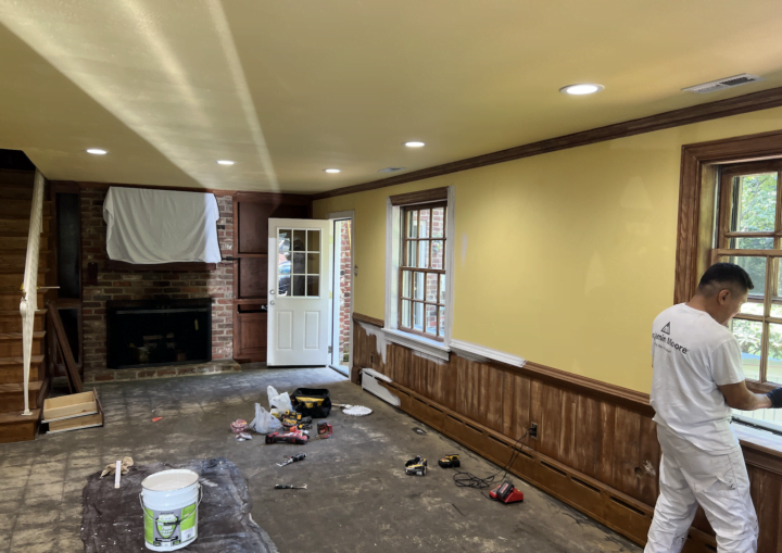 A man wearing a white painting outfit paints the trim of a window transforming it from brown to white