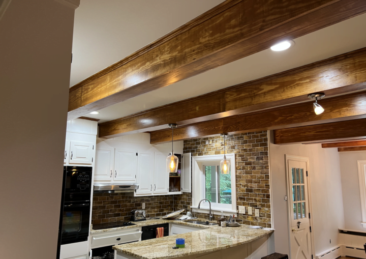 A kitchen with white walls and white cabinets framed by granite counter tops and rustic wooden beams