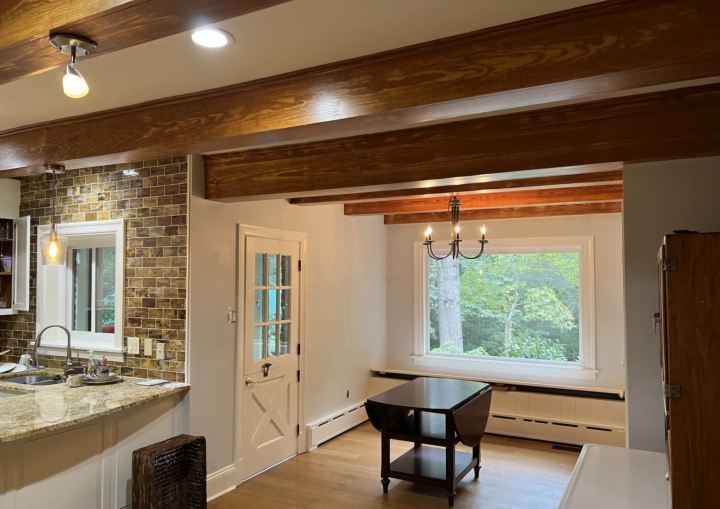A kitchen with white walls and white cabinets framed by granite counter tops and rustic wooden beams
