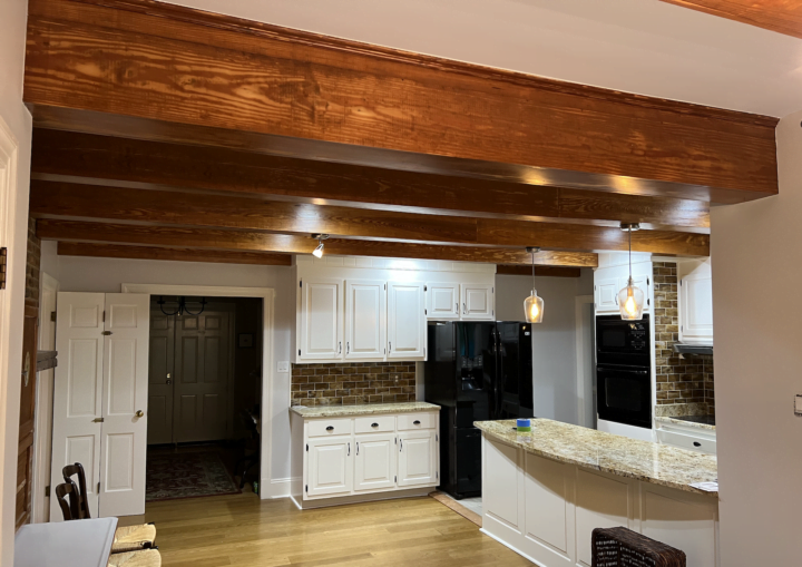 A kitchen with white walls and white cabinets framed by granite counter tops and rustic wooden beams