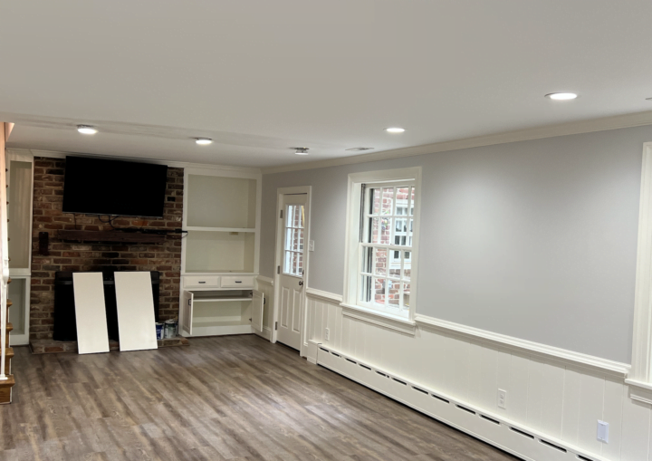 A living room with grey walls, white wainscoting and white built ins with a television and brick fireplace