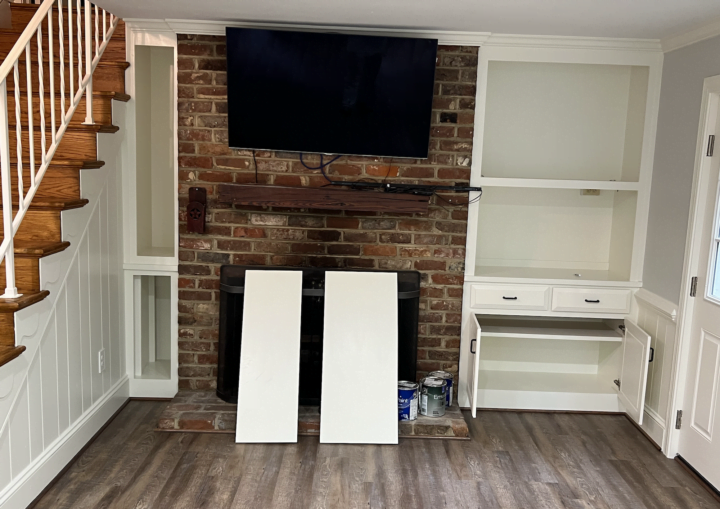 A living room with grey walls and white built ins with a television and brick fireplace
